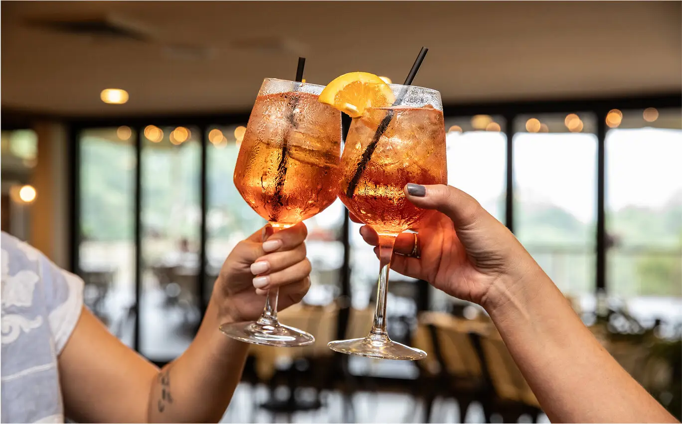 Two vibrant cocktails served in tall glasses at The Hef&rsquo;s Hut, showcasing colorful layers and fresh garnishes.