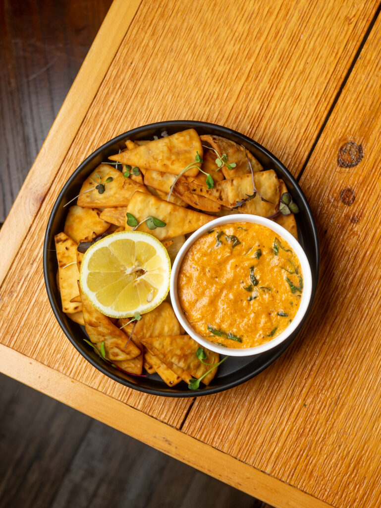 A plate of tortillas with dipping sauce and a lemon wedge.