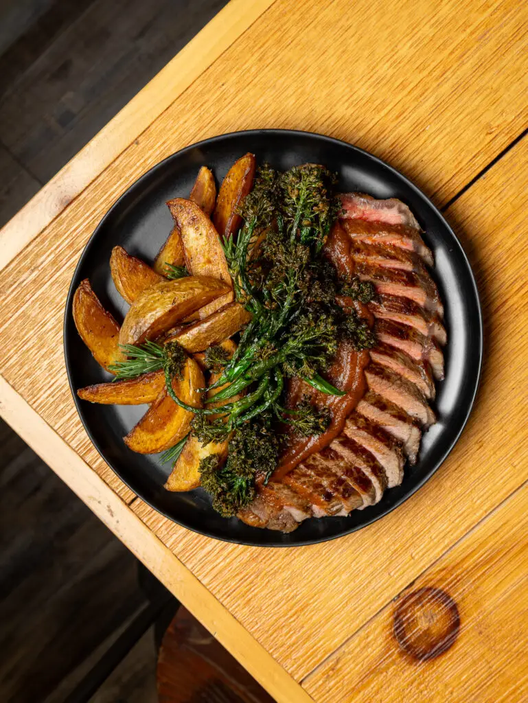 A cooked steak served with crispy potato wedges on a plate. smoked meat in North Jersey